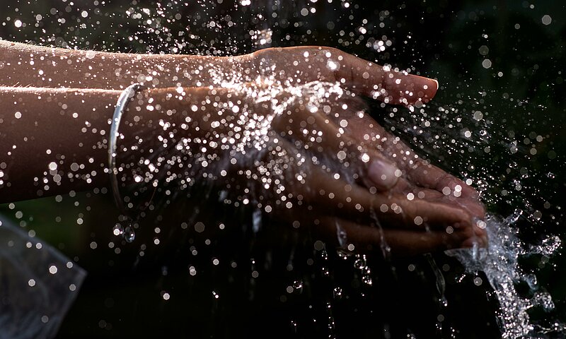 Wasser das aus einer Quelle auf 2 Hände spritzt.