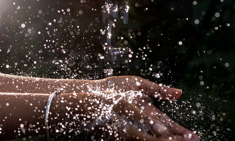 Wasser das aus einer Quelle auf 2 Hände spritzt.