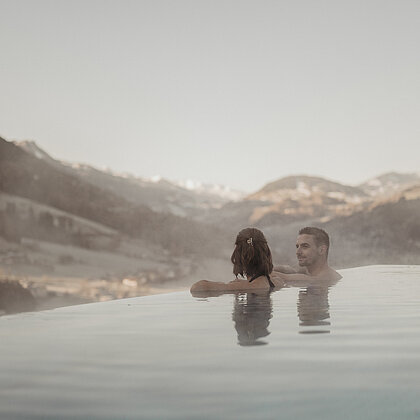 Paar genießt den Infinity-Pool mit Blick auf die Salzburger Berglandschaft im Hotel Berghof.
