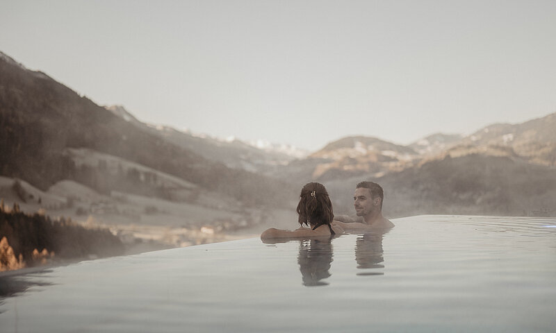 Paar genießt den Infinity-Pool mit Blick auf die Salzburger Berglandschaft im Hotel Berghof.