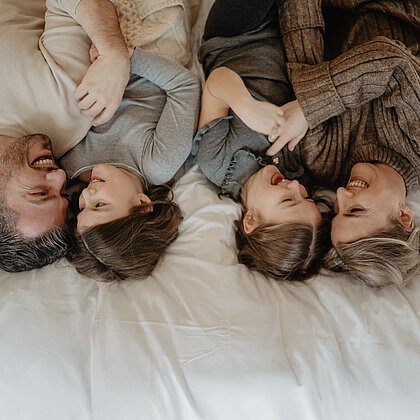 Familie lacht und kuschelt liegend im Bett.