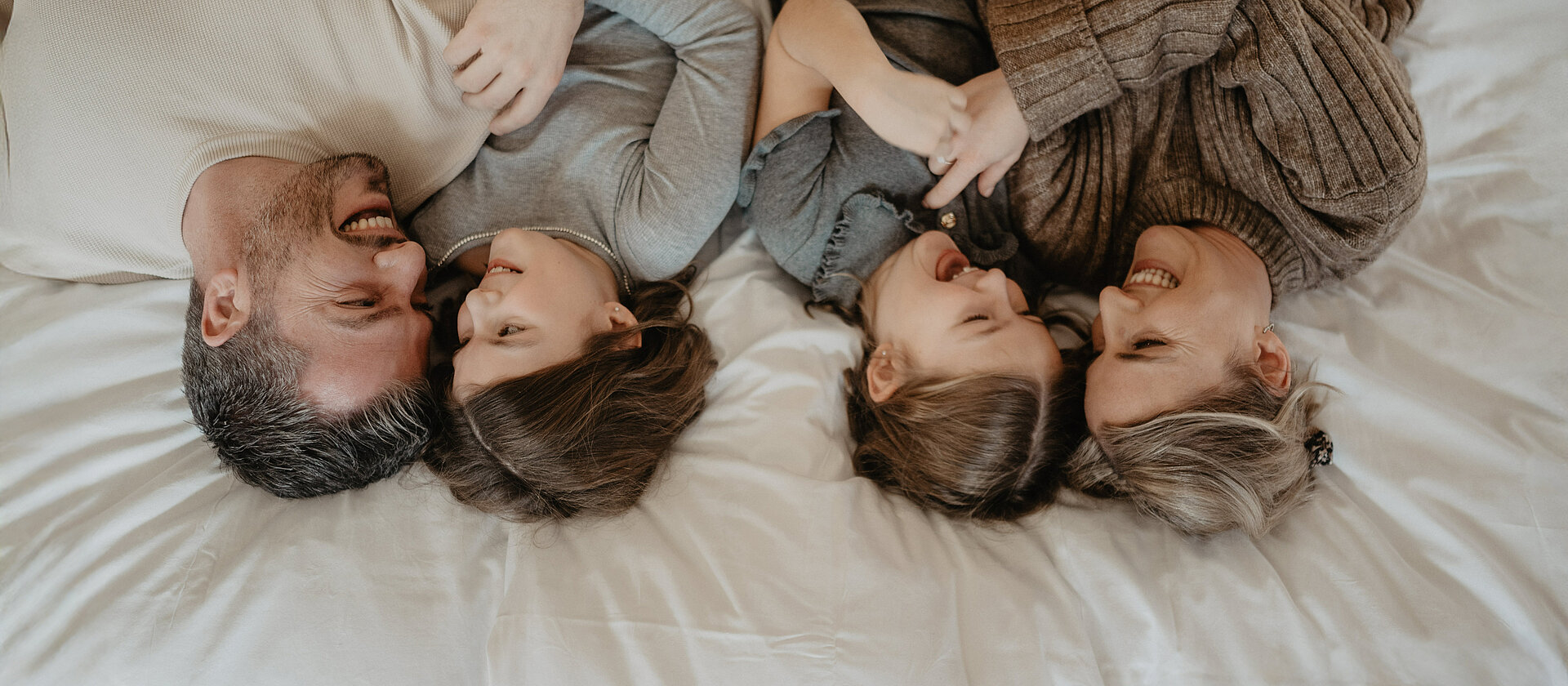 Familie lacht und kuschelt liegend im Bett.