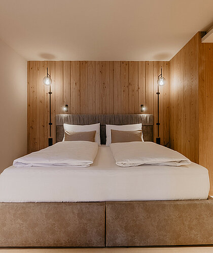 Schlafbereich der Top Familiensuite mit Holzpaneelen, Boxspringbett und elegantem Design im Hotel Berghof Salzburg.
