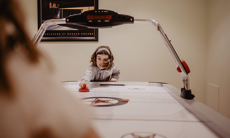 Ein Kind spielt Airhockey im Gamingroom des Hotel Berghofs.