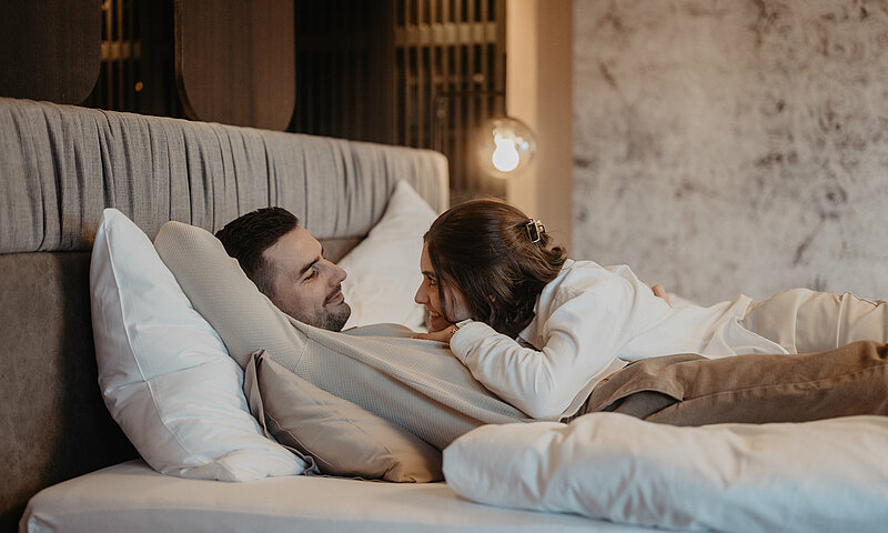 Ein Paar liegt gemeinsam im Bett und sieht sich verträumt an.