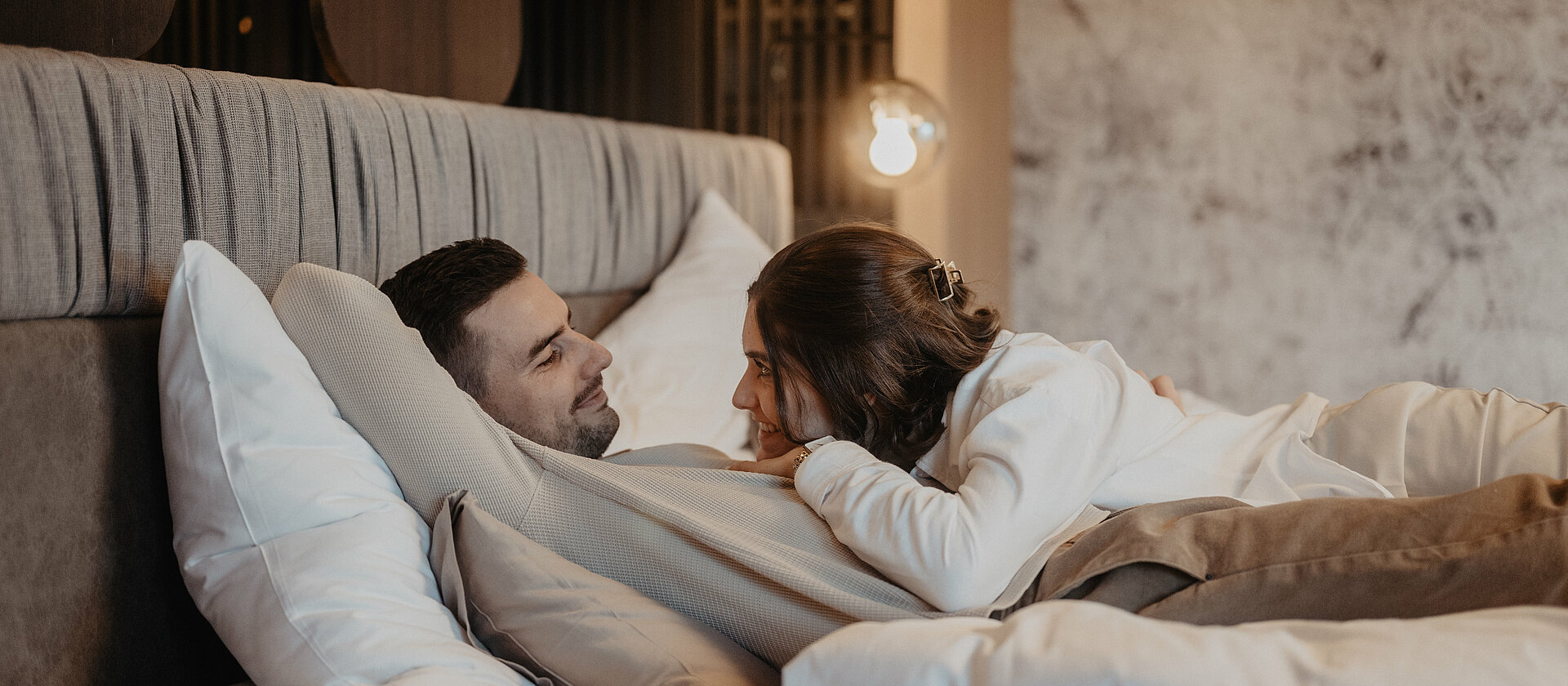 Ein Paar liegt gemeinsam im Bett und sieht sich verträumt an.