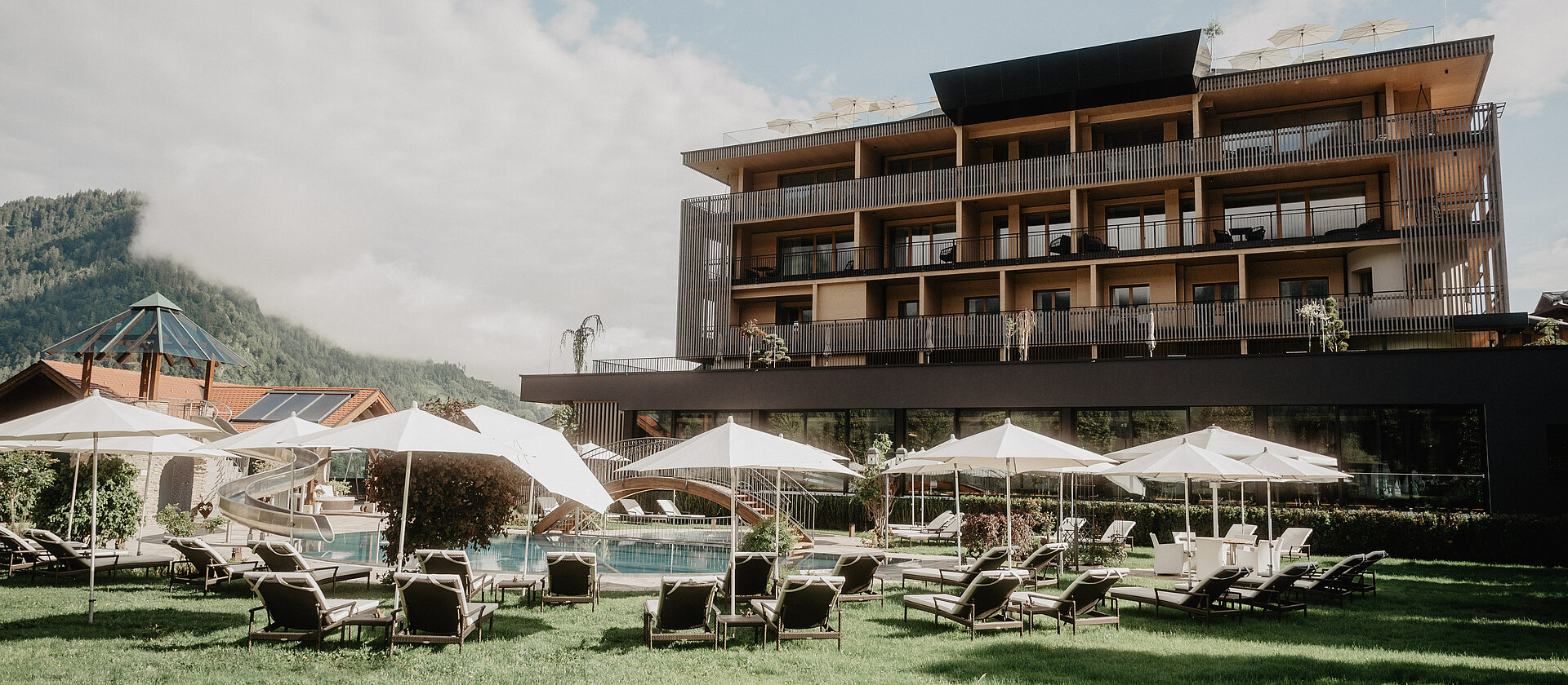 Liegewiese mit Sonnenliegen und Sonnenschirmen vor dem Hotel Berghof Salzburg an einem sonnigen Sommertag.
