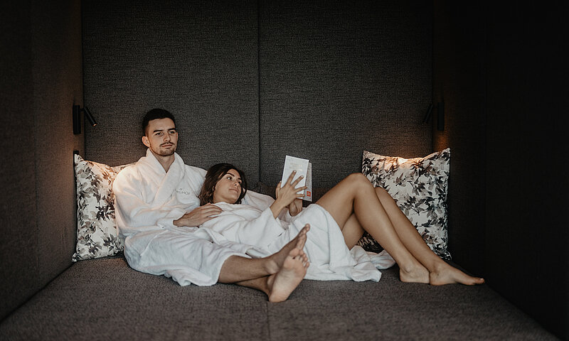 Paar entspannt im stilvollen Ruheraum des Hotel Berghof in Salzburg und liest ein Buch.