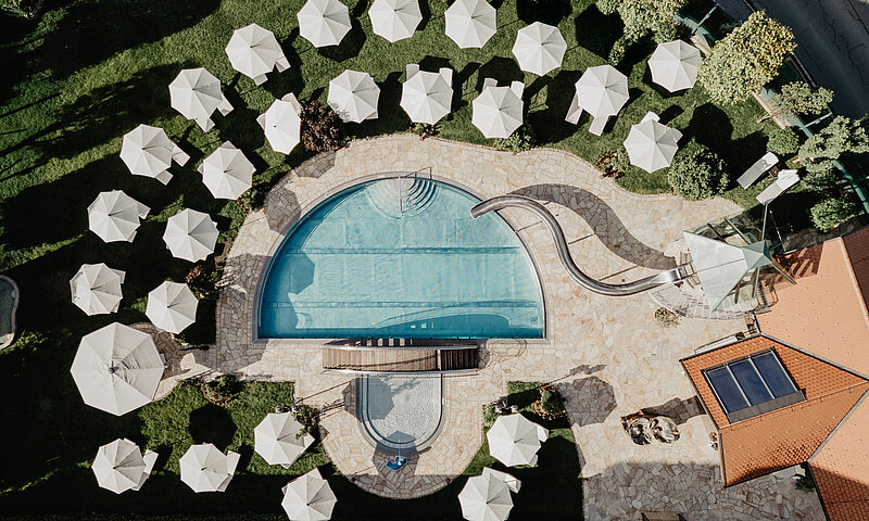 Luftaufnahme des Pools mit Sonnenschirmen und Liegen im Hotel Berghof Salzburg.