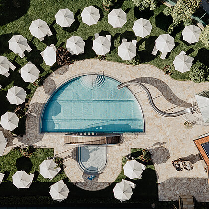 Luftaufnahme des Pools mit Sonnenschirmen und Liegen im Hotel Berghof Salzburg.