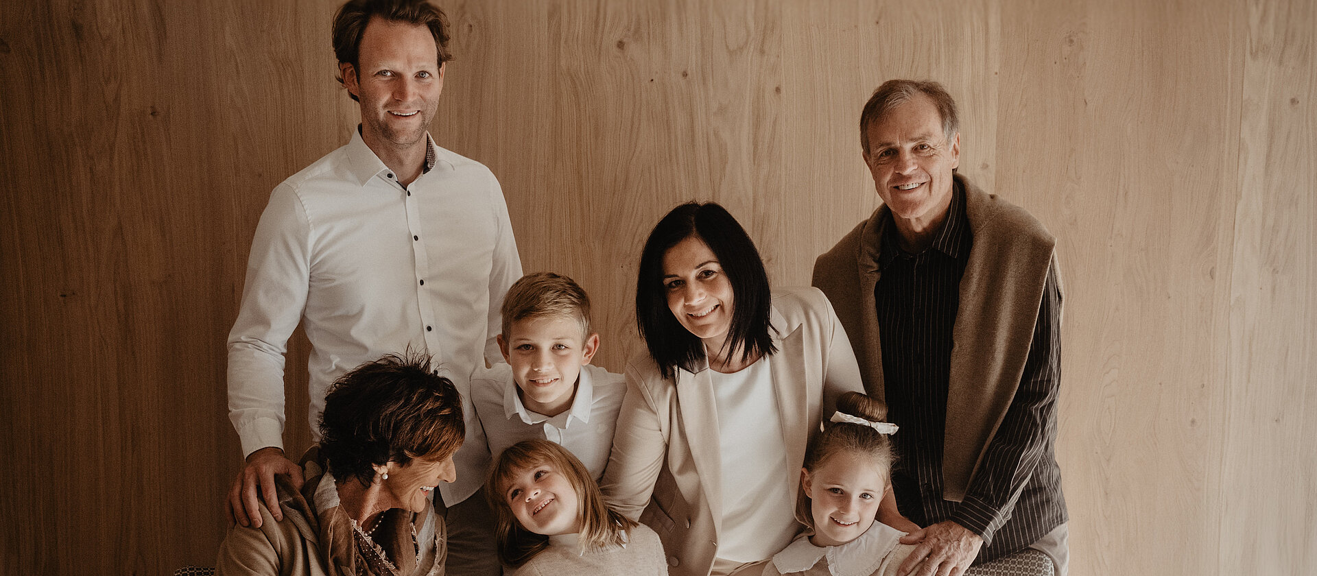 Familienfoto der Familie Rettenwender, alle drei Generationen in heller Bekleidung vor einer Holzwand