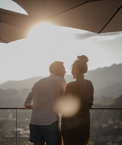 Paar genießt den Sonnenuntergang am Balkon mit Bergblick.