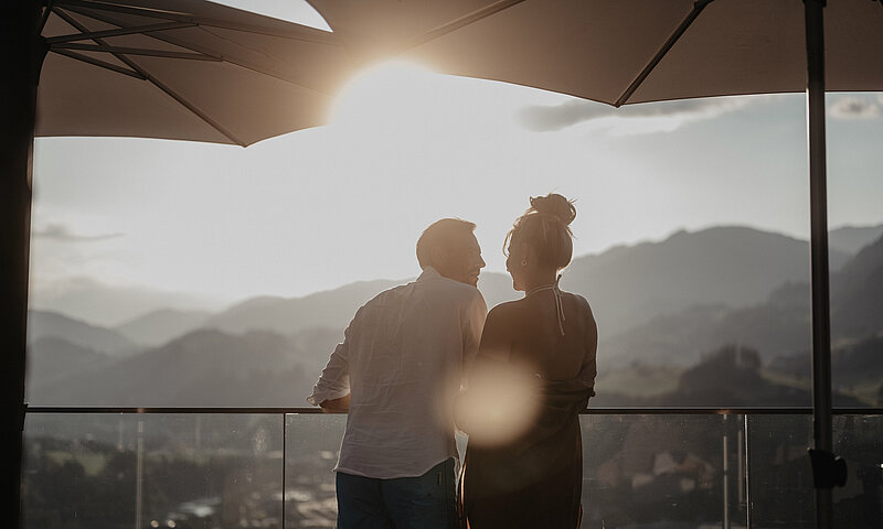 Paar genießt den Sonnenuntergang am Balkon mit Bergblick.