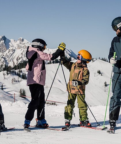 Eine Familie fährt Ski in St. Johann im Pongau und die Kinder geben sich ein High Five.