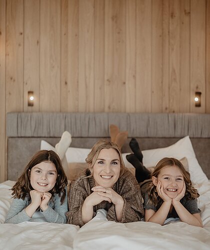 Eine Mutter mit zwei Töchtern liegt im Bett im Hotel Berghof.