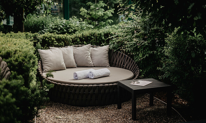 Gemütliche Liegeinsel mit Kissen und Handtüchern inmitten des Naturgartens im Romantik- und Wellnesshotel Berghof in Salzburg.