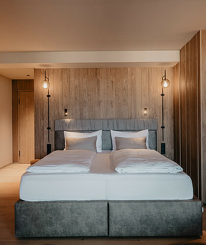 Schlafbereich der Berghof Suite Premium mit großem Doppelbett, Holzverkleidung und stilvollem Ambiente im Hotel Berghof Salzburg.