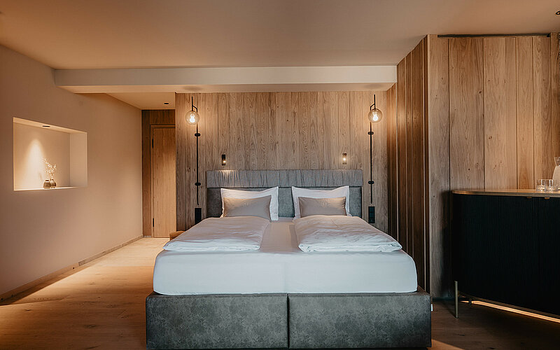 Schlafbereich der Berghof Suite Premium mit großem Doppelbett, Holzverkleidung und stilvollem Ambiente im Hotel Berghof Salzburg.