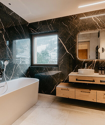 Geräumiges Badezimmer der Top Familiensuite mit Badewanne, Doppelwaschtisch und Fensterblick im Hotel Berghof Salzburg.