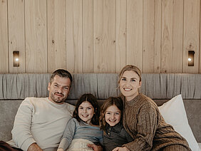 Eltern kuscheln im Boxspringbett mit ihren beiden Töchtern.