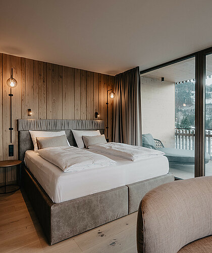 Hochwertig gestalteter Schlafbereich der Panorama Suite Premium mit großem Doppelbett, Holzwandverkleidung und Panoramafenstern im Hotel Berghof in Salzburg.