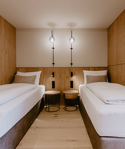 Zwei komfortable Einzelbetten, mit Möglichkeit auf ein Zusatzbett, mit Boxspringmatratzen in der Premium Familiensuite, modern gestaltet mit Holzverkleidung.