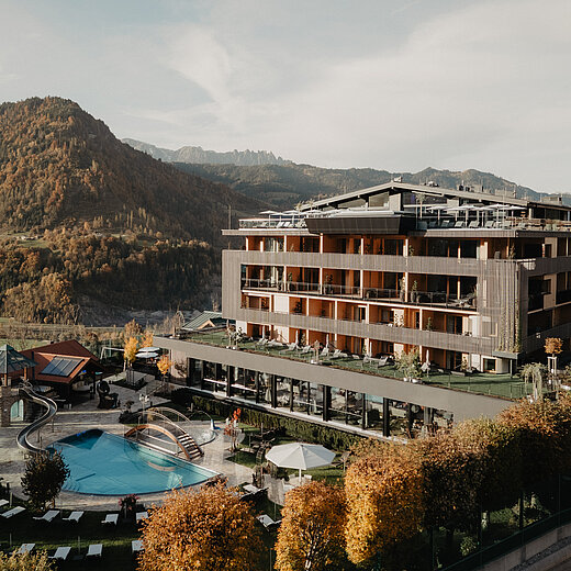 Hotel Berghof im Alpendorf mit Outdoor Pool und Blick auf die herbstliche Berglandschaft.