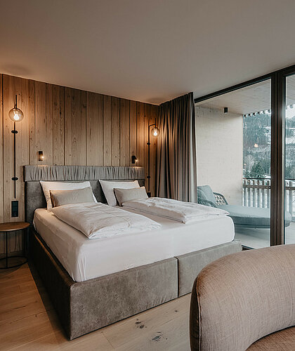 Hochwertig gestalteter Schlafbereich der Panorama Suite Premium mit großem Doppelbett, Holzwandverkleidung und Panoramafenstern im Hotel Berghof in Salzburg.