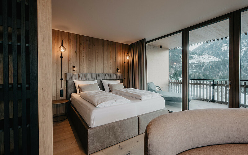 Hochwertig gestalteter Schlafbereich der Panorama Suite Premium mit großem Doppelbett, Holzwandverkleidung und Panoramafenstern im Hotel Berghof in Salzburg.
