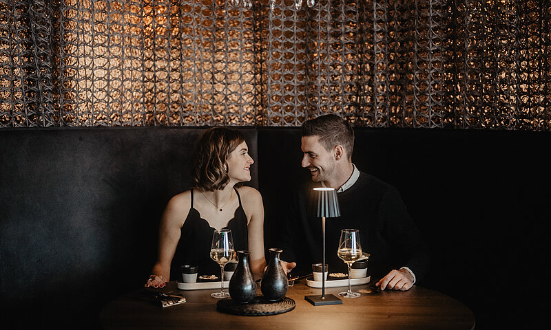 Zwei Personen schauen sich verliebt an vor dunkler Kulisse im Restaurant Medusa im Hotel Berghof.