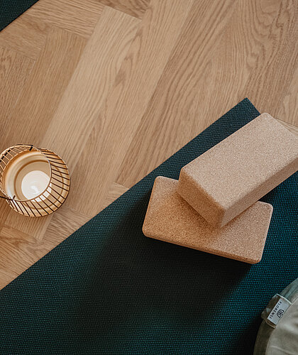 Detailaufnahme von Yoga-Accessoires wie Korkblöcke, Meditationskissen und Kerzen auf einer Yogamatte im Hotel Berghof, Salzburg.