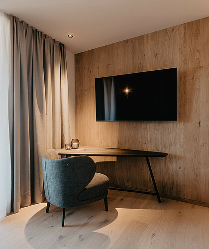 Arbeitsbereich der Berghof Suite Premium mit Schreibtisch, Sessel und Flachbildfernseher im Hotel Berghof Salzburg.