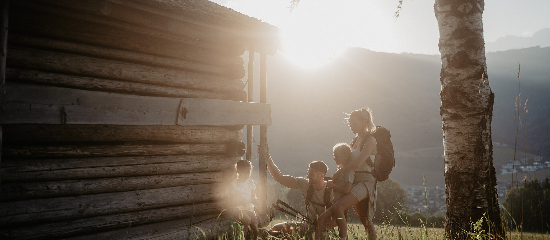 Eine Familie legt eine Pause ein vom Wandern mit einem traumhaften Sonnenuntergang im Hintergrund.