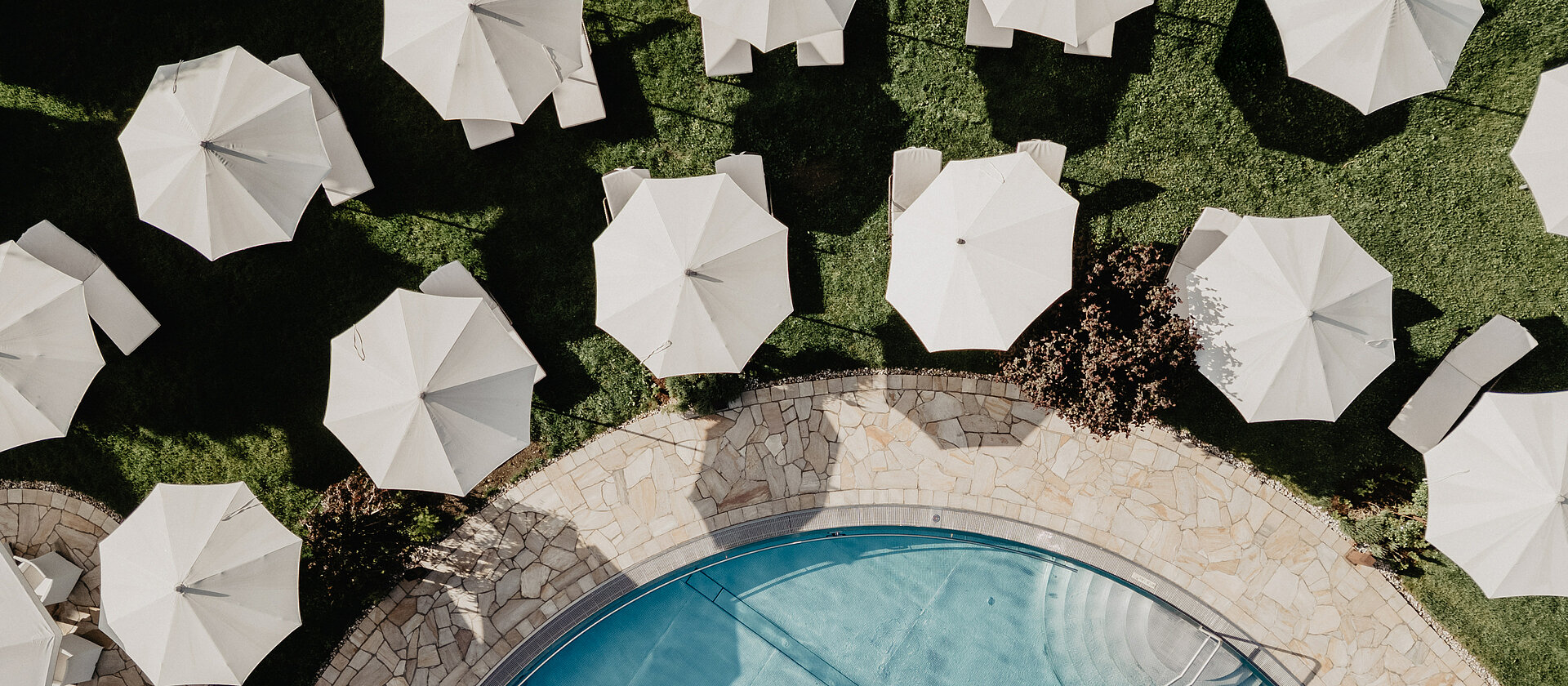 Sonnenschirme und Liegen am Poolbereich des Hotel Berghof Salzburg aus der Vogelperspektive.