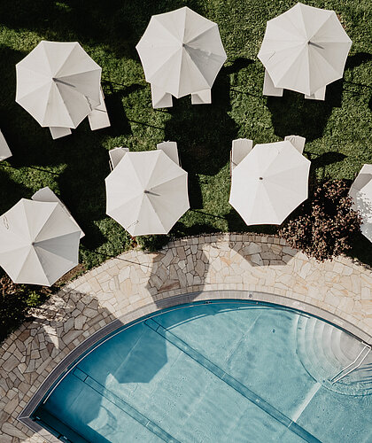 Sonnenschirme und Liegen am Poolbereich des Hotel Berghof Salzburg aus der Vogelperspektive.