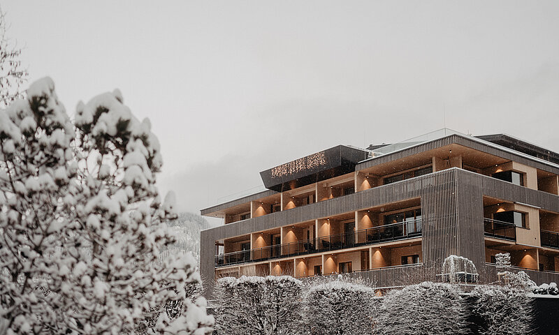 Winterliche Ansicht des modernen Hotel Berghof in St. Johann in Salzburg, umgeben von verschneiten Bäumen und Bergen in Österreich.