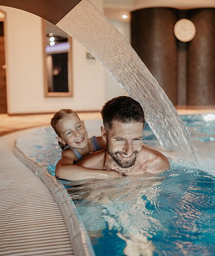 Vater mit Kind beim gemeinsamen Schwimmen im Indoor-Pool des Hotel Berghof in St. Johann im Pongau.