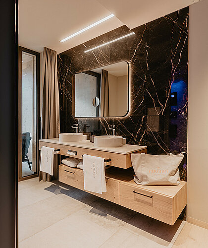 Modernes Badezimmer der Top Familiensuite mit Doppelwaschtisch, Marmorfliesen und eleganter Beleuchtung im Hotel Berghof Salzburg.