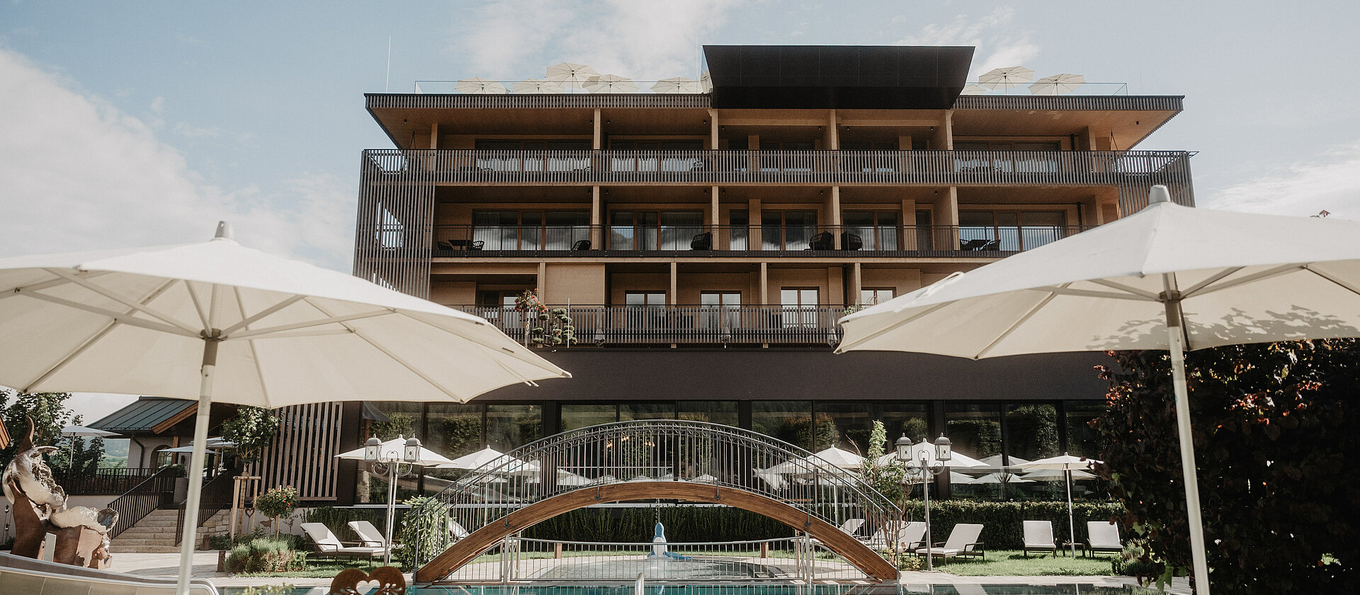 Poolbereich mit Brücke, Sonnenschirmen und Hotelgebäude im Hintergrund.