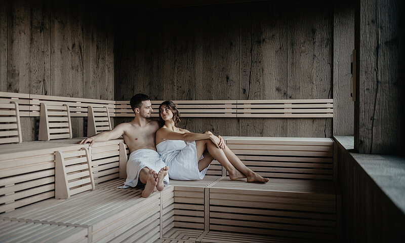 Paar sitzt entspannt in der modernen Sauna mit Holzinterieur im Hotel Berghof in Salzburg.