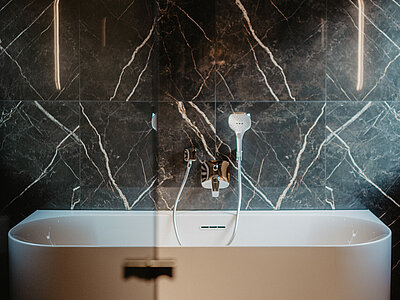 Elegante freistehende Badewanne in einem modernen Badezimmer mit edler schwarzer Marmorwand.