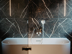 Elegante freistehende Badewanne in einem modernen Badezimmer mit edler schwarzer Marmorwand.