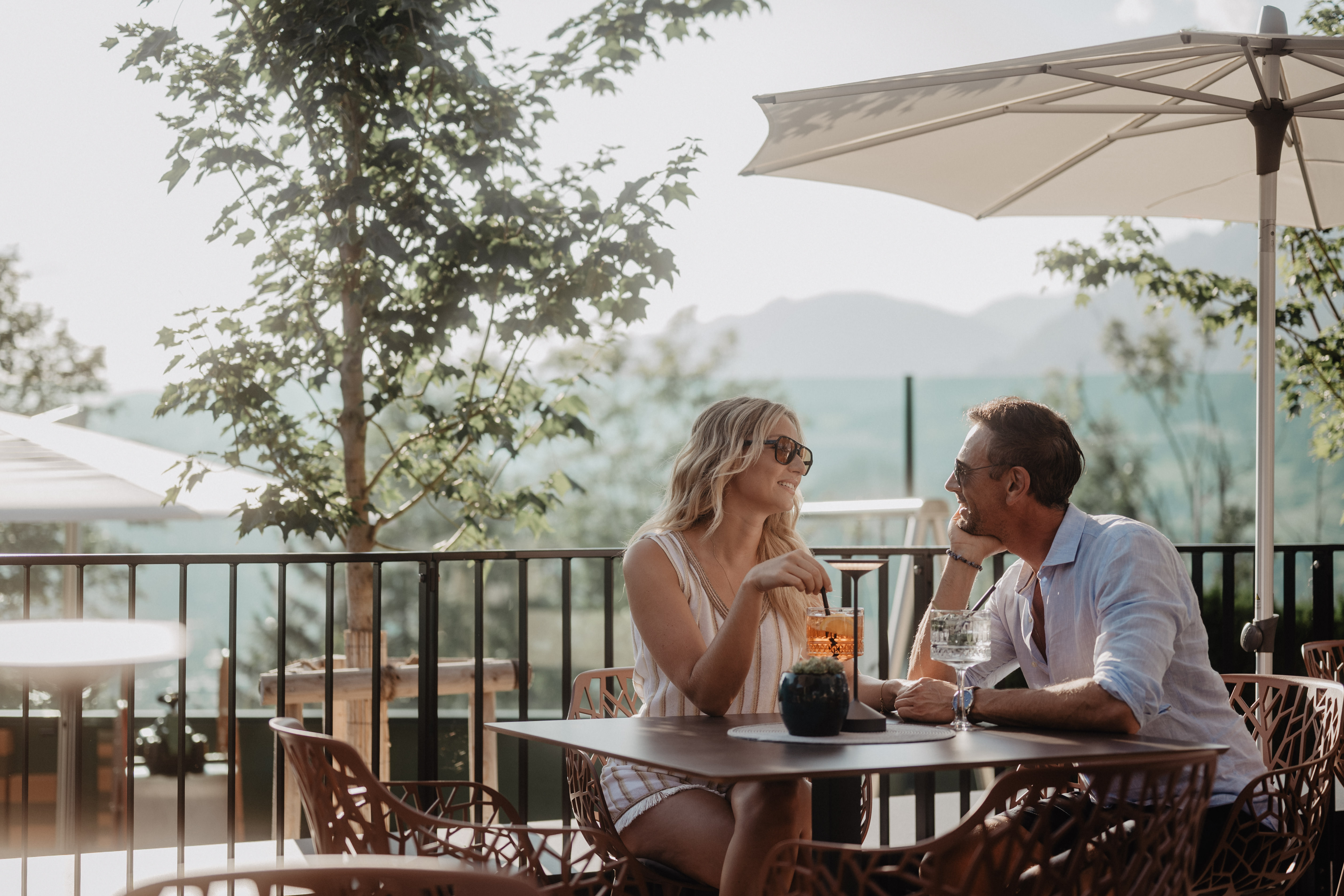 Ein Paar sitzt auf der Panoramaterrasse des Hotel Berghof und genießt Drinks im Sonnenschein.
